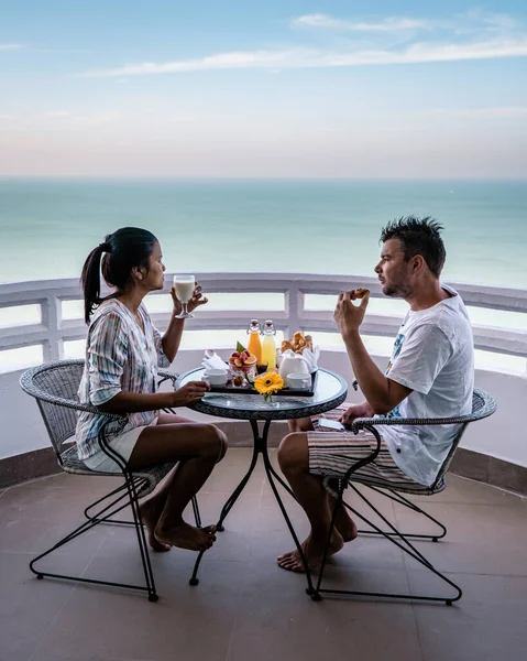 Pareja desayunando en balcón con vistas al océano, mujer asiática y hombre de Europa de vacaciones en Tailandia —  Fotos de Stock