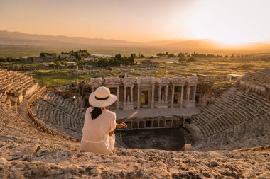Hierapolis antik kenti Pamukkale Türkiye, Unesco harabelerinde günbatımını izleyen şapkalı genç kadın