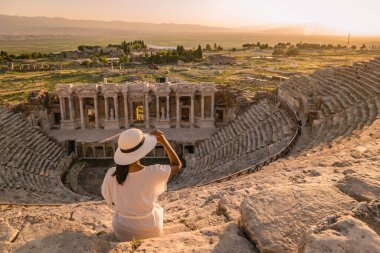 Hierapolis antik kenti Pamukkale Türkiye, Unesco harabelerinde günbatımını izleyen şapkalı genç kadın