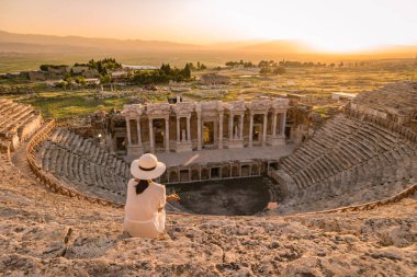 Hierapolis antik kenti Pamukkale Türkiye, Unesco harabelerinde günbatımını izleyen şapkalı genç kadın