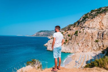 Kaputas Beach Kas hindisi, Kas Turkey nehrinin kıyısındaki kayalıklardan beyaz turuncu plaj, uçurumun kenarında duran okyanus manzaralı adamlar.