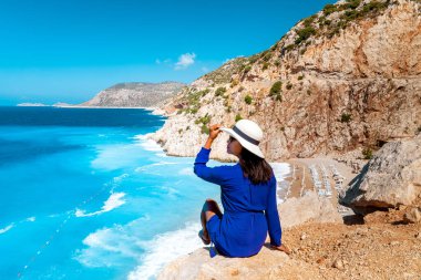 Kaputas Beach Kas hindisi, Kas Turkey nehrinin kıyısındaki kayalıklardan beyaz turuncu plaj, uçurumun kenarında duran okyanus manzaralı kadın.