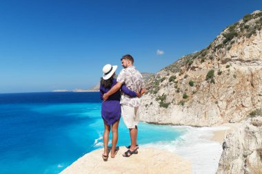 Türkiye 'de tatil yapan çift, Kaputas Beach Kas hindisi, Kas Turkey nehrinin kıyısındaki kayalıklardan beyaz turuncu plaj, uçurumun kenarında duran kadın ve erkekler okyanusa bakıyor.