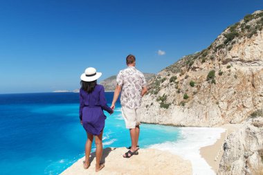 Türkiye 'de tatil yapan çift, Kaputas Beach Kas hindisi, Kas Turkey nehrinin kıyısındaki kayalıklardan beyaz turuncu plaj, uçurumun kenarında duran kadın ve erkekler okyanusa bakıyor.