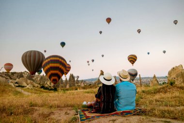 Gündoğumunda Kapadokya Türkiye, Goreme Kapadokya tepelerinde tatil yapan iki orta yaşlı erkek ve kadın, Kapadokya 'da sıcak hava balonlarıyla güneşlenen erkek ve kadın