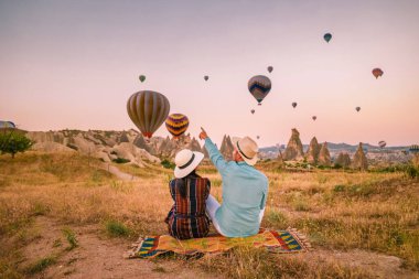 Gündoğumunda Kapadokya Türkiye, Goreme Kapadokya tepelerinde tatil yapan iki orta yaşlı erkek ve kadın, Kapadokya 'da sıcak hava balonlarıyla güneşlenen erkek ve kadın