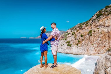 Türkiye 'de tatil yapan çift, Kaputas Beach Kas hindisi, Kas Turkey nehrinin kıyısındaki kayalıklardan beyaz turuncu plaj, uçurumun kenarında duran kadın ve erkekler okyanusa bakıyor.