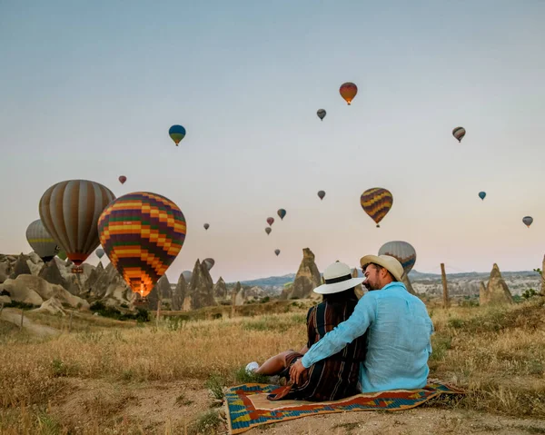 Capadocia Turquía durante el amanecer, pareja hombres y mujeres de mediana edad de vacaciones en las colinas de Goreme Capadocia Turquía, hombres y mujeres mirando sunrsise con globos de aire caliente en Capadocia —  Fotos de Stock