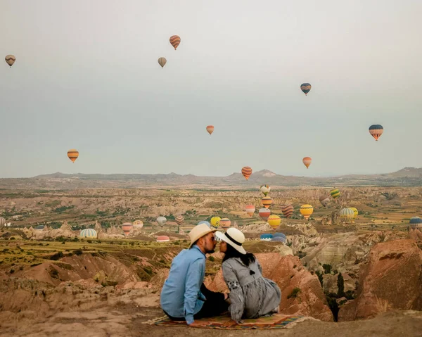 在日出期间，土耳其卡帕多西亚，一对中年男女在土耳其哥雷姆卡巴多西亚山区度假，男人和女人在卡帕多西亚拿着热气球晒太阳 — 图库照片