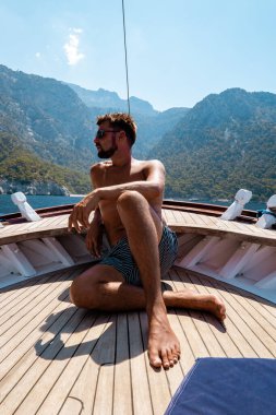 Fethiye Türkiye 'deki Kelebek plajına tekne gezisi sırasında tahta bir teknede dinlenen genç adam, mayo giymiş bronzlaşmış genç çocuk