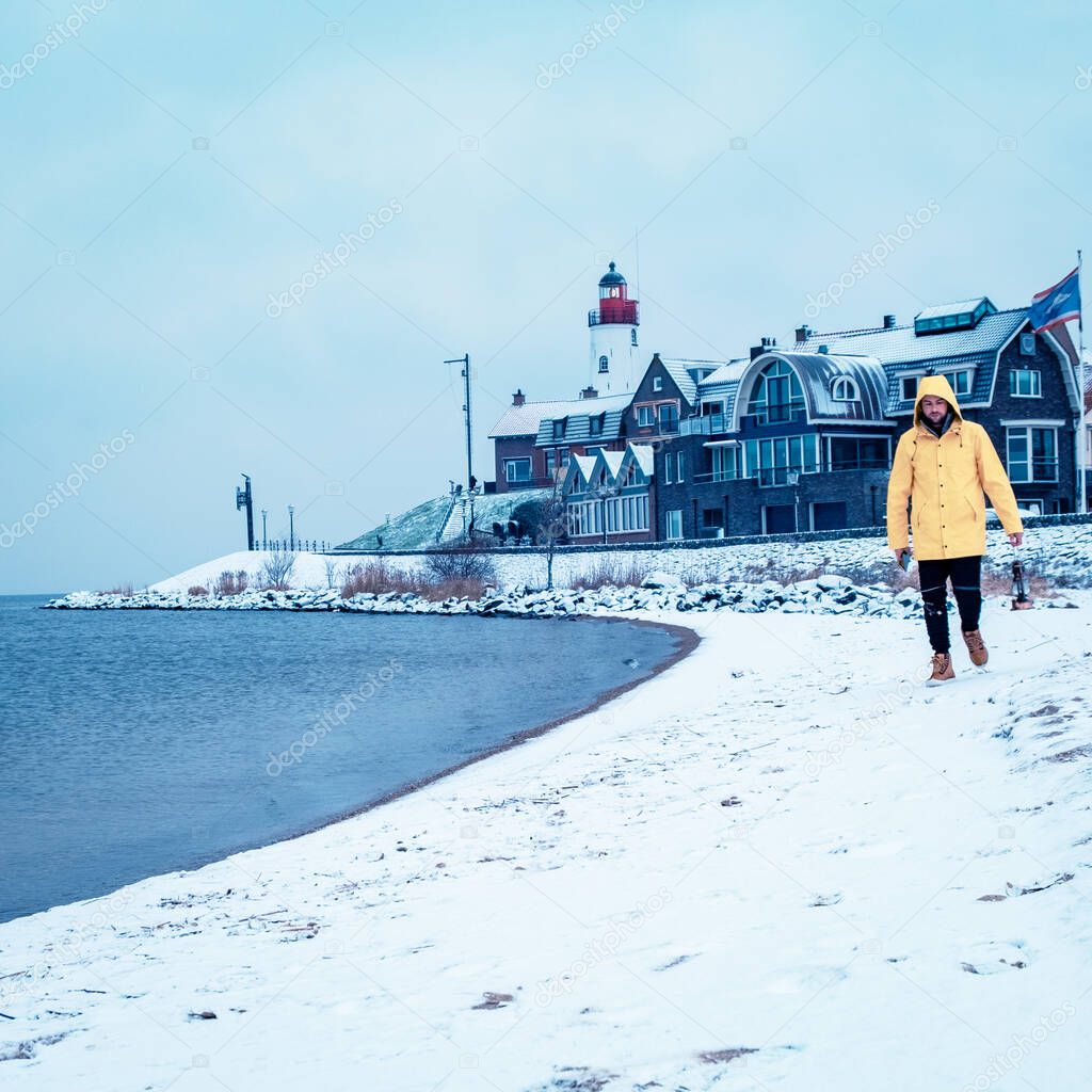 young men in yellow rain jacket walking on a snowy beach by the lighthouse of Urk Netherlands, men with oil lamp and ranin coat