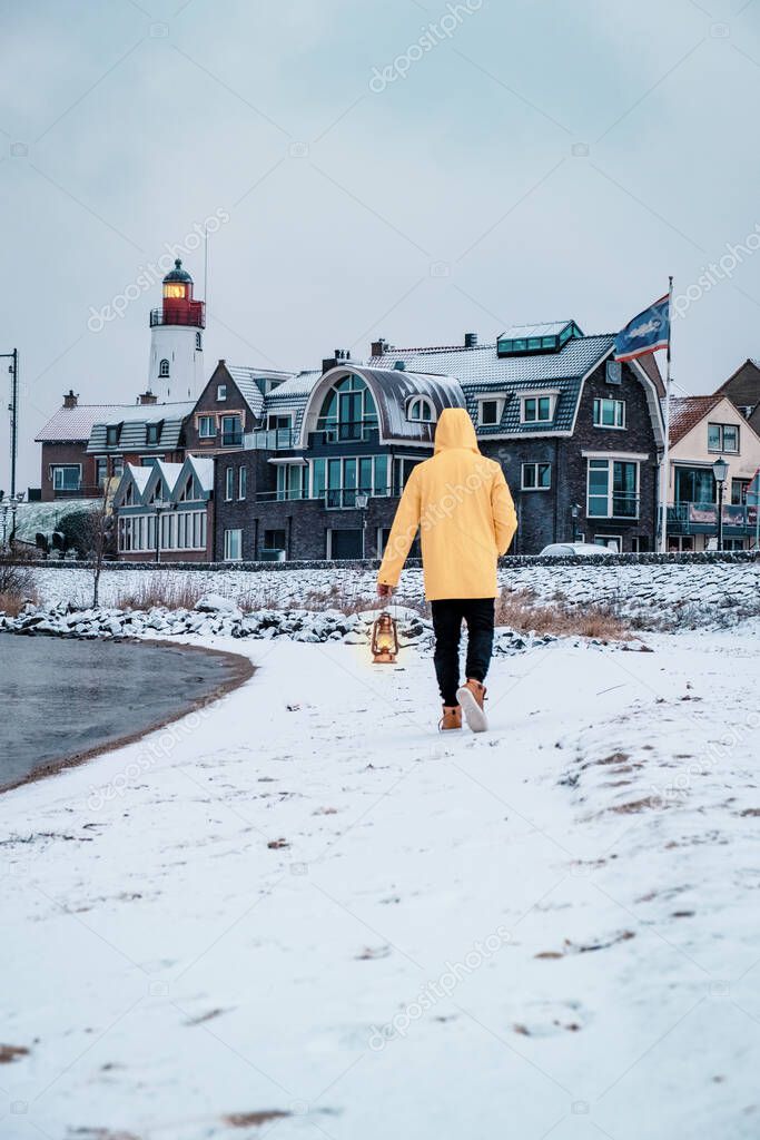 young men in yellow rain jacket walking on a snowy beach by the lighthouse of Urk Netherlands, men with oil lamp and ranin coat