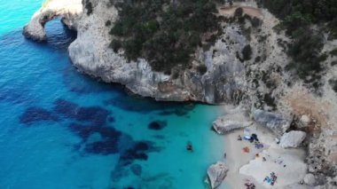 Sardinya Adası İtalya Orosei kıyıları, plaj şemsiyeleriyle dolu güzel bir sahil manzarası, güneşlenen ve turkuaz bir suda yüzen insanlar. Cala Gonone, Sardinya, İtalya, Cala Mariolu