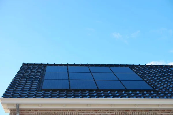 Новый дом в Нидерландах с солнечными панелями, установленными на крыше на фоне солнечного неба Закрытие нового здания черными солнечными панелями — стоковое фото