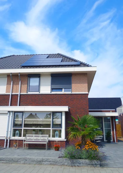 Новый дом в Нидерландах с солнечными панелями, установленными на крыше на фоне солнечного неба Закрытие нового здания черными солнечными панелями — стоковое фото