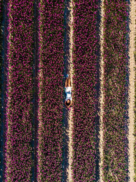 Dutch tulip field, woman with dress and summer hat in tulips field Netherlands,happy young woman in pink flower field