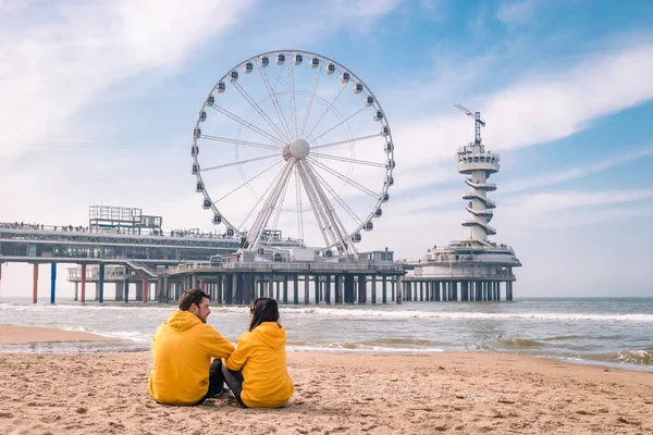 Pár na pláži Schevening Netherlands během jara, The Ferris Wheel The Pier u Scheveningenu v Holandsku, slunečný jarní den na pláži — Stock fotografie
