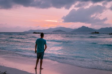 La Digue Seyşeller, tropikal adada açık mavi okyanusla beyaz sahilde yürüyen genç adamlar.