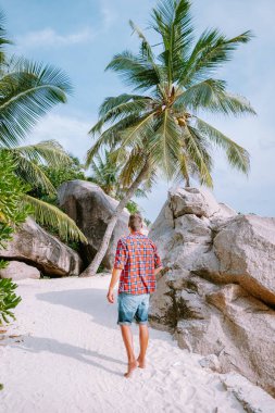 La Digue Seyşeller, tropikal adada açık mavi okyanusla beyaz sahilde yürüyen genç adamlar.