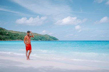 Cote DOr Sahili, Praslin Seyşeller tropikal adası, beyaz sahilde yüzen genç erkekler büyük kayalar ve kayalar ve tatil sırasında palmiye ağaçları olan beyaz tropikal bir plaj.