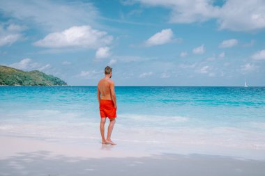 Cote DOr Sahili, Praslin Seyşeller tropikal adası, beyaz sahilde yüzen genç erkekler büyük kayalar ve kayalar ve tatil sırasında palmiye ağaçları olan beyaz tropikal bir plaj.