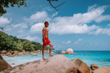 Cote DOr Sahili, Praslin Seyşeller tropikal adası, beyaz sahilde yüzen genç erkekler büyük kayalar ve kayalar ve tatil sırasında palmiye ağaçları olan beyaz tropikal bir plaj.