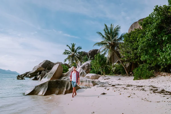 ラ・ディグ・セイシェル熱帯の島で休暇中に澄んだ青い海と白いビーチを歩く若い男性 — ストック写真