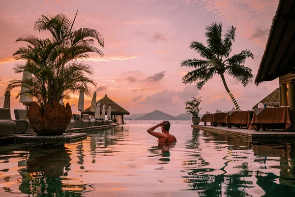 Młodzi mężczyźni w basenie o zachodzie słońca, Luksusowy basen w tropikalnym kurorcie, relaksujący wypoczynek na Seszelach. La Digue, Młody człowiek podczas zachodu słońca przy basenie — Zdjęcie stockowe