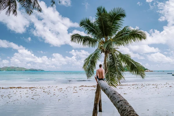 Cote DOr Beach, Praslin Seychellen tropische eiland, jonge mannen in zwemmen kort op het witte strand met enorme rotsblokken en rotsen en een wit tropisch strand met palmbomen tijdens vakantie Seychellen — Stockfoto