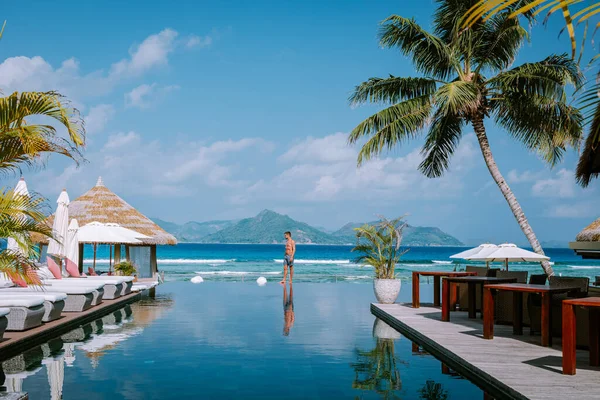 Jeunes hommes dans la piscine au coucher du soleil, piscine de luxe dans une station tropicale, vacances relaxantes dans les îles Seychelles. La Digue, Jeune homme au coucher du soleil près de la piscine — Photo