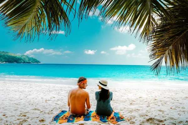 Tropikalna biała plaża na wyspie Praslin Seszele, szczęśliwa Młoda para mężczyzna i kobieta podczas wakacji na plaży relaksujący się pod palmą — Zdjęcie stockowe