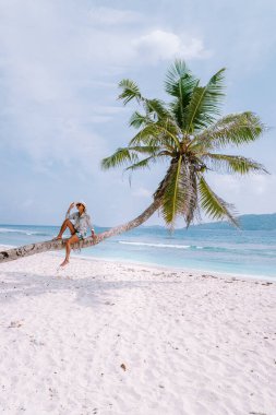 La Digue Seyşeller, beyaz tropikal plajda gün batımı palmiye ağacıyla, Seyşeller 'de tatilde olan genç bir kadın, beyaz sahildeki lüks tatil yeri kızı.