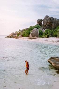 La Digue Seyşeller, beyaz tropikal plajda gün batımı palmiye ağacıyla, Seyşeller 'de tatilde olan genç bir kadın, beyaz sahildeki lüks tatil yeri kızı.