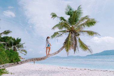 La Digue Seyşeller, beyaz tropikal plajda gün batımı palmiye ağacıyla, Seyşeller 'de tatilde olan genç bir kadın, beyaz sahildeki lüks tatil yeri kızı.