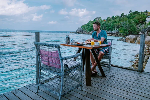 세이셸 LA 디그 아일랜드 에서 아침 식사를 하며 바다를 바라보고 있는 젊은 남자 — 스톡 사진