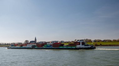 Lobith Hollanda, Nisan 2020, Nehir gergedanındaki büyük konteynır gemisi. Nehirde güneşli bir bahar gününde, içinde renkli konteynırlar bulunan Almanya yakınlarında.