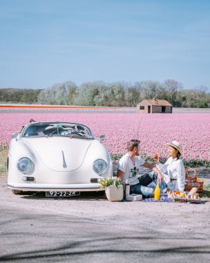Lisse Hollanda 'da. Çift eski bir spor arabayla yolculuğa çıkıyor. Beyaz Porsche 356 Speedster, Hollanda çiçek soğanı bölgesi lale tarlalarıyla.