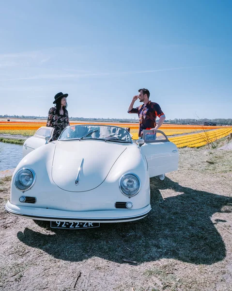 Lisse Netherlands,. pareja haciendo un viaje por carretera con un viejo coche deportivo vintage White Porsche 356 Speedster, región de bulbos de flores holandesas con campos de tulipanes — Foto de Stock