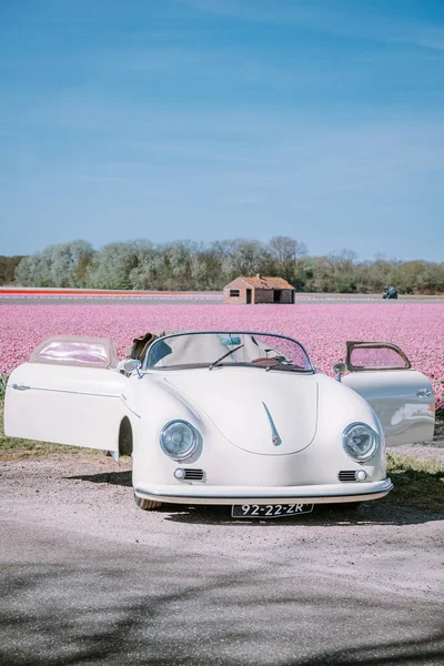 Lisse Netherlands,. pareja haciendo un viaje por carretera con un viejo coche deportivo vintage White Porsche 356 Speedster, región de bulbos de flores holandesas con campos de tulipanes — Foto de Stock