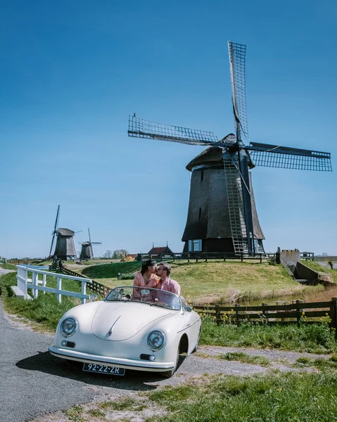 Schermerhorn Alkmaar Netherlands Апрель 2020,. Пара, путешествующая со старым винтажным спортивным автомобилем White Porsche 356 Speedster, голландская ветряная мельница деревня Шермерхорн — стоковое фото
