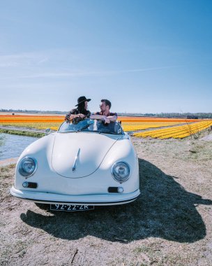 Lisse Hollanda 'da. Çift eski bir spor arabayla yolculuğa çıkıyor. Beyaz Porsche 356 Speedster, Hollanda çiçek soğanı bölgesi lale tarlalarıyla.