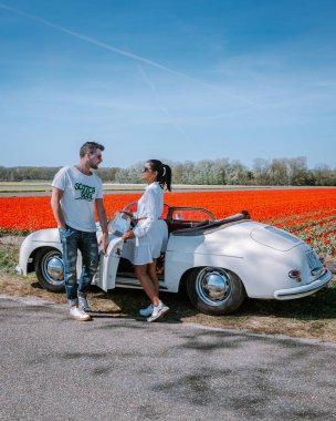 Lisse Hollanda 'da. Çift eski bir spor arabayla yolculuğa çıkıyor. Beyaz Porsche 356 Speedster, Hollanda çiçek soğanı bölgesi lale tarlalarıyla.