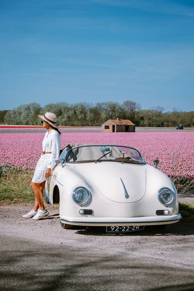 Lisse Netherlands,. pareja haciendo un viaje por carretera con un viejo coche deportivo vintage White Porsche 356 Speedster, región de bulbos de flores holandesas con campos de tulipanes — Foto de Stock