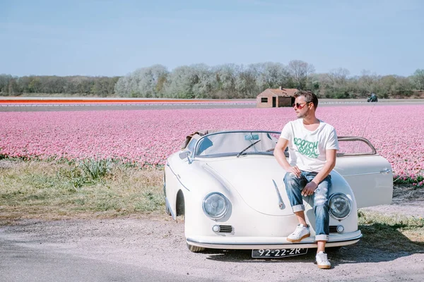 Lisse Netherlands,. casal fazendo uma viagem com um velho carro esporte vintage Branco Porsche 356 Speedster, holandês região bulbo flor com campos de tulipa — Fotografia de Stock