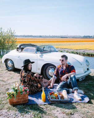 Lisse Hollanda 'da. Çift eski bir spor arabayla yolculuğa çıkıyor. Beyaz Porsche 356 Speedster, Hollanda çiçek soğanı bölgesi lale tarlalarıyla.