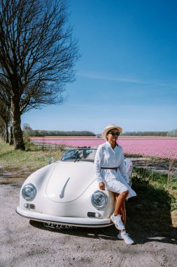 Lisse Hollanda 'da. Çift eski bir spor arabayla yolculuğa çıkıyor. Beyaz Porsche 356 Speedster, Hollanda çiçek soğanı bölgesi lale tarlalarıyla.
