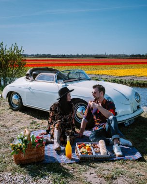 Lisse Hollanda 'da. Çift eski bir spor arabayla yolculuğa çıkıyor. Beyaz Porsche 356 Speedster, Hollanda çiçek soğanı bölgesi lale tarlalarıyla.