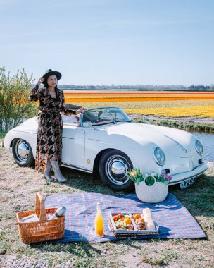 Lisse Hollanda 'da. Çift eski bir spor arabayla yolculuğa çıkıyor. Beyaz Porsche 356 Speedster, Hollanda çiçek soğanı bölgesi lale tarlalarıyla.