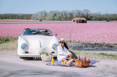 Lisse Hollanda 'da. Çift eski bir spor arabayla yolculuğa çıkıyor. Beyaz Porsche 356 Speedster, Hollanda çiçek soğanı bölgesi lale tarlalarıyla.