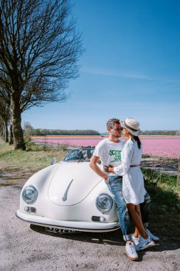 Lisse Hollanda 'da. Çift eski bir spor arabayla yolculuğa çıkıyor. Beyaz Porsche 356 Speedster, Hollanda çiçek soğanı bölgesi lale tarlalarıyla.